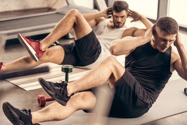 Handsome sportsmen doing sit ups together in gym — Stock Photo