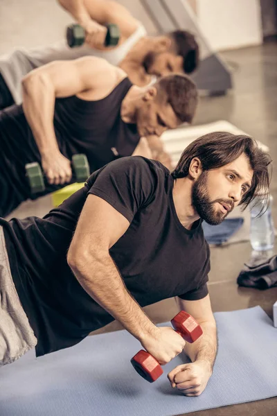 Beaux sportifs s'entraînent simultanément avec des haltères sur le sol dans la salle de gym — Photo de stock