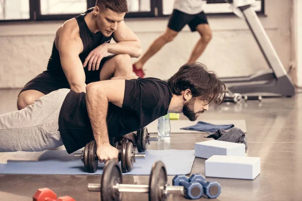 Seitenansicht eines gut aussehenden Sportlers, der Liegestütze auf Hanteln im Fitnessstudio macht — Stockfoto