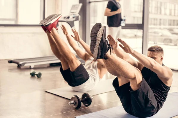 Deportistas ejercitándose simultáneamente sobre colchonetas de yoga en el gimnasio - foto de stock