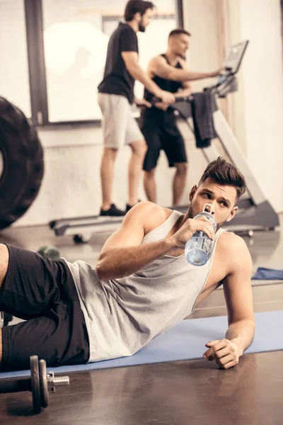 Desportista bonito beber água de garrafa no ginásio — Fotografia de Stock