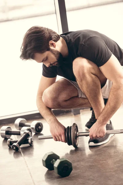 Schöner Sportler legt Hantelscheiben auf Eisenstange für das Training im Fitnessstudio — Stockfoto