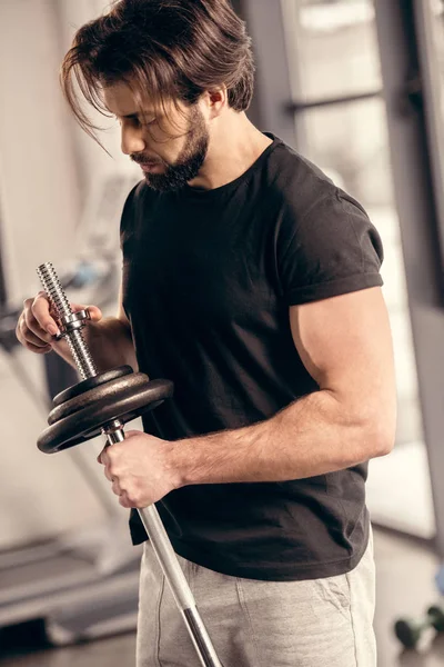 Handsome sportsman fixing weight plates on iron bar for training in gym — Stock Photo