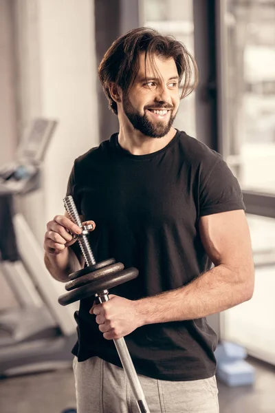 Усміхнений красивий спортсмен фіксує вагові пластини на залізному барі для тренувань у спортзалі — стокове фото