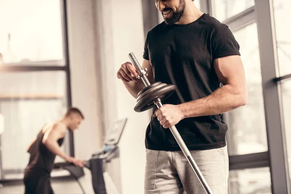 Обрезанный образ спортсмена, закрепляющего тяжелые пластины на железной штанге для тренировок в тренажерном зале — стоковое фото