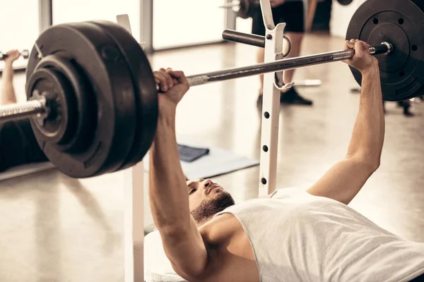 Belo desportista levantar barbell com placas de peso pesado no ginásio — Stock Photo