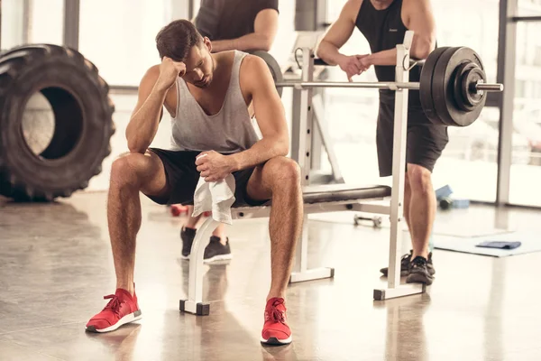 Bonito cansado desportista sentado e descansando no supino no ginásio — Stock Photo