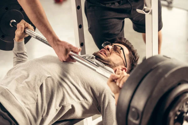 Image recadrée de l'entraîneur aidant sportif haltère de levage avec des poids lourds dans la salle de gym — Photo de stock