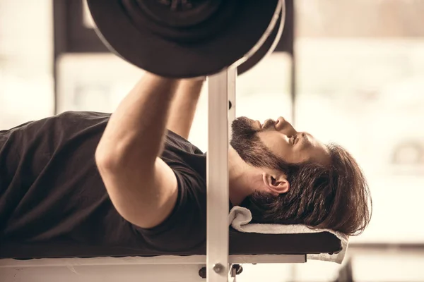 Side view of handsome sportsman lifting barbell with weight plates in gym — Stock Photo