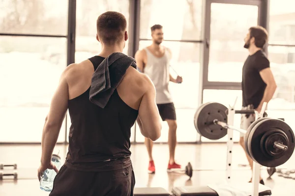 Вид сзади мускулистого мужчины, смотрящего на друзей в спортзале — стоковое фото
