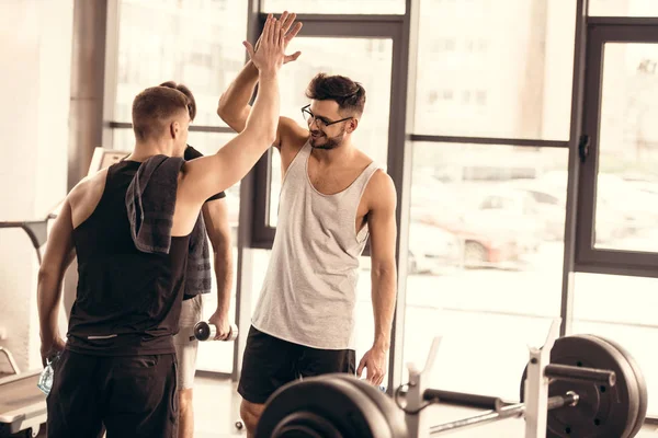 Guapos deportistas alegres dando cinco en el gimnasio - foto de stock