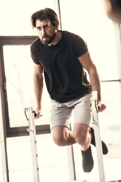 Full length view if athletic young man in sportswear exercising on bars in gym — Stock Photo