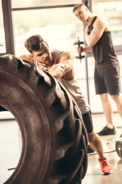 Atlético joven en ropa deportiva ejercicio con neumático en el gimnasio — Stock Photo