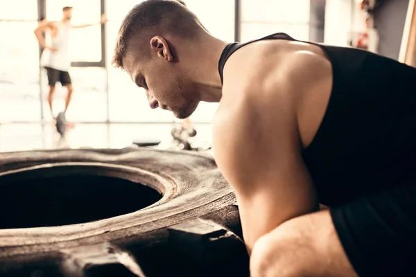 Side view of muscular young sportsman exercising with tire in gym — Stock Photo