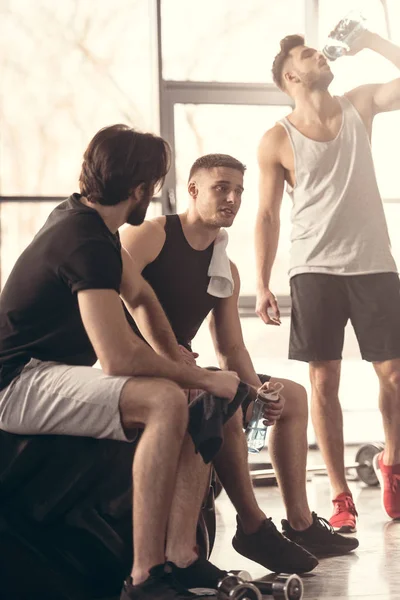 Young sportsmen sitting on tire and talking after workout in gym — Stock Photo