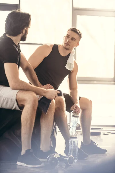 Two young sportsmen sitting on tire and looking at each other after workout in gym — Stock Photo