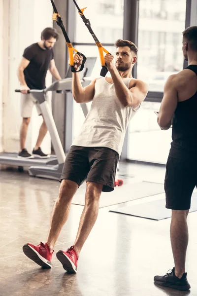 Vue complète de l'entraînement sportif des jeunes hommes avec des bandes de résistance dans la salle de gym — Photo de stock