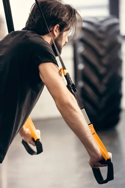 Vue latérale de l'entraînement sportif des jeunes hommes avec des sangles de fitness dans la salle de gym — Photo de stock