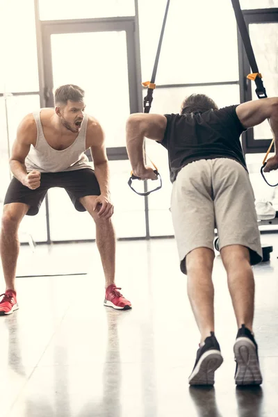 Trainer yelling at sportsman exercising with resistance bands in gym — Stock Photo