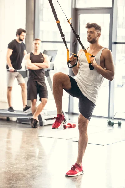 Vue complète de l'entraînement musculaire des jeunes hommes avec des bandes de résistance dans le centre sportif — Photo de stock