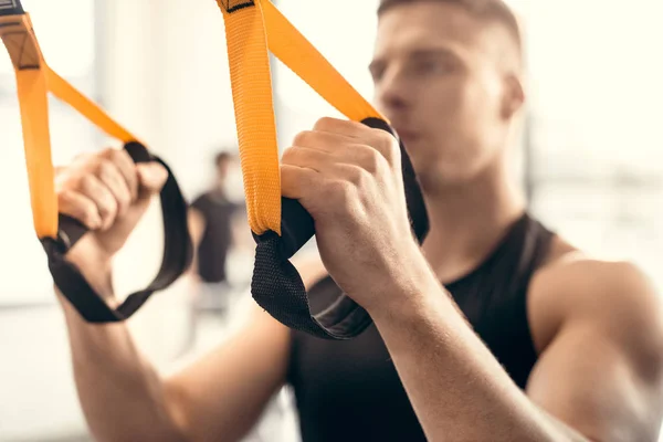 Vista de cerca del entrenamiento muscular de hombre joven con correas de suspensión en el gimnasio - foto de stock