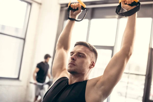 Schöner junger Mann trainiert mit Federbeinen und schaut im Fitnessstudio weg — Stockfoto