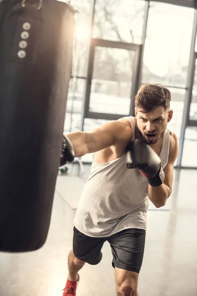 Entraînement émotionnel jeune sportif avec sac de boxe dans la salle de gym — Photo de stock