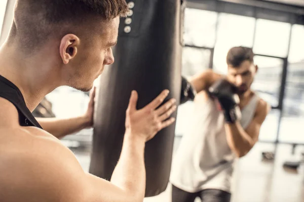 Erschossener Mann hält Boxsack, während Boxer in Turnhalle zuschlägt — Stockfoto