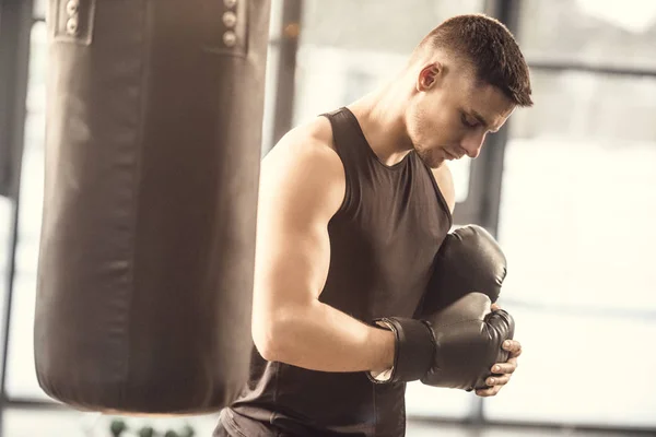 Side view of muscular sportsman wearing boxing gloves in gym — Stock Photo