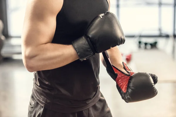 Обрезанный кадр мускулистого спортсмена в боксёрских перчатках в спортзале — стоковое фото