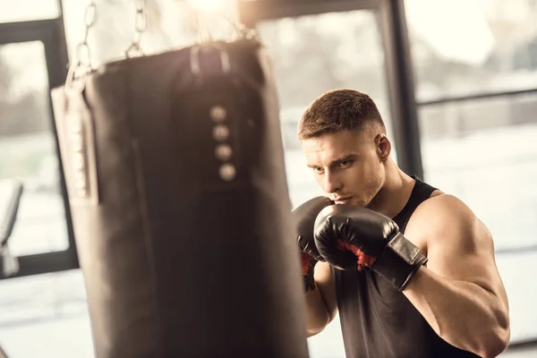 Atlético jovem em luvas de boxe treinamento com saco de perfuração no ginásio — Fotografia de Stock