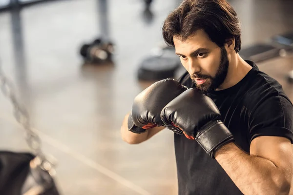 Handsome focused young man in boxing gloves exercising in sports center — Stock Photo