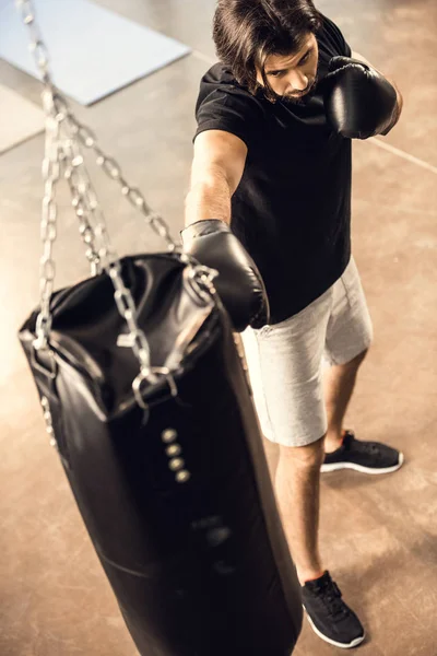 Visão de alto ângulo de desportivo jovem boxe com saco de perfuração no ginásio — Fotografia de Stock