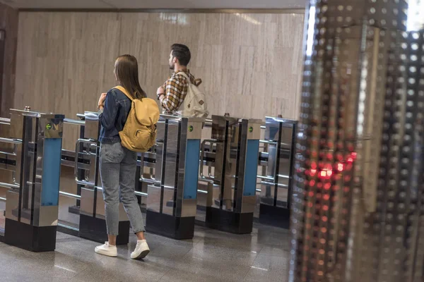 Rear view of couple of stylish tourists with backpacks passing through turnstiles — Stock Photo