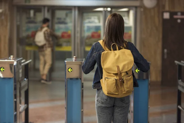 Rear view of female stylish traveler with backpack passing through turnstiles and male tourist behind — Stock Photo