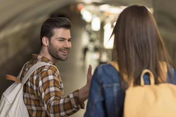Smiling male tourist with backpack giving hand to girlfriend at subway station — Stock Photo