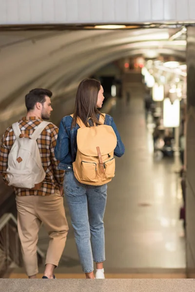 Rear view of couple of stylish travelers with backpacks at subway station — Stock Photo