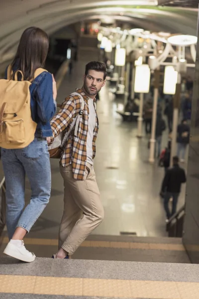 Paar stylische Touristen mit Rucksäcken halten sich an der Hand und gehen zur U-Bahn-Station — Stockfoto