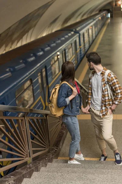 Stylish travelers with backpacks standing on stairs at subway station — Stock Photo