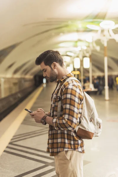 Vista lateral del hombre con mochila y smartphone en la estación de metro - foto de stock