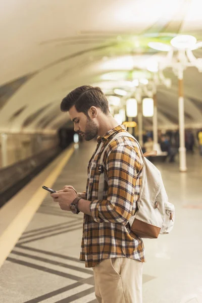 Side view of man with backpack and smartphone at metro station — Stock Photo