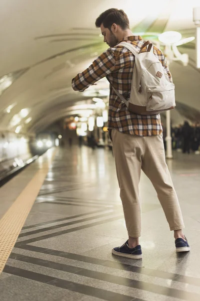 Hombre con mochila mirando el reloj de pulsera en la estación de metro - foto de stock