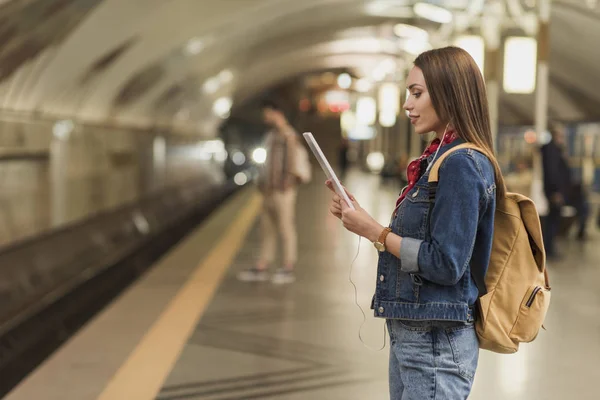 Side view of stylish woman with earphones and digital tablet at metro station — Stock Photo