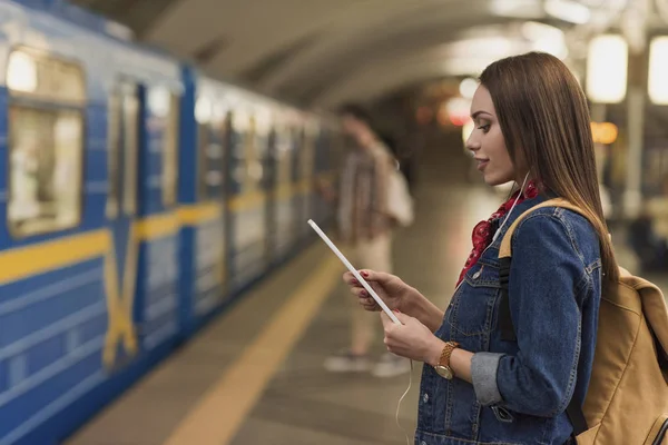 Young woman with earphones and digital tablet at metro station — Stock Photo
