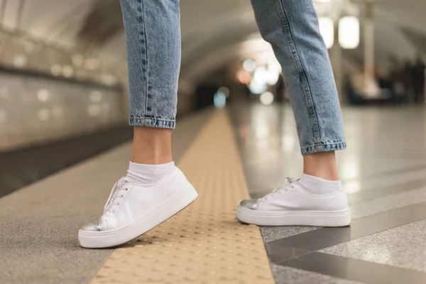 Immagine ritagliata di gambe femminili in jeans alla moda e scarpe da ginnastica alla stazione della metropolitana — Foto stock