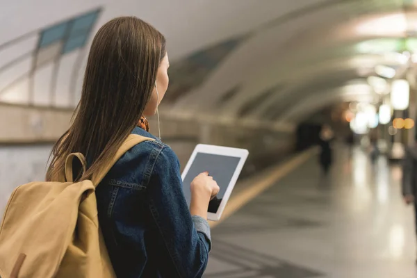 Vue arrière de la femme élégante avec tablette numérique et écouteurs à la station de métro — Photo de stock