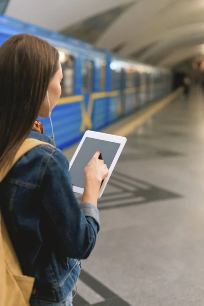 Vue arrière de la femme élégante avec écouteurs et tablette numérique à la station de métro — Photo de stock