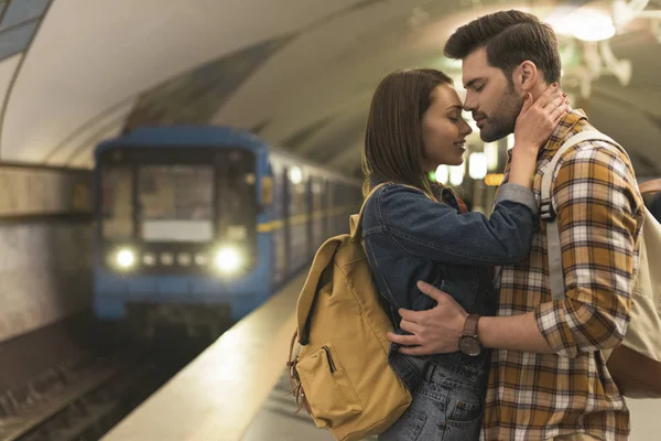 Vista lateral de casal elegante de viajantes abraçando uns aos outros na estação de metrô — Fotografia de Stock