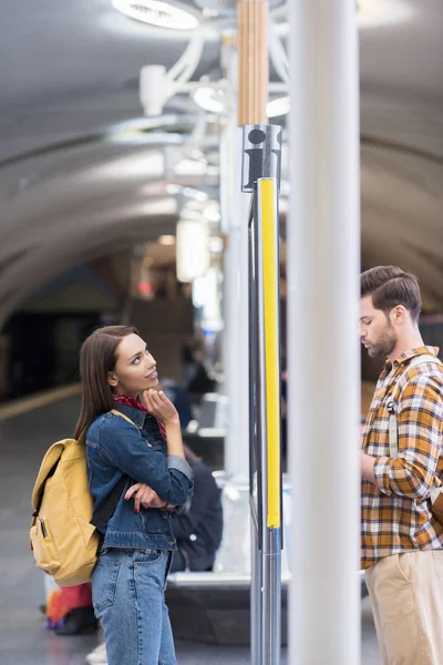 Vista lateral de mujer turista sonriente mirando tablero de información y novio con teléfono inteligente - foto de stock