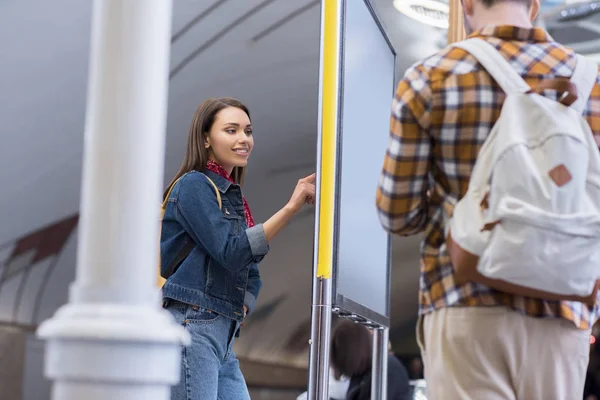 Vista trasera de turista masculino con mochila y su novia mirando el tablero de información en la estación de metro — Stock Photo